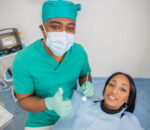 Happy dentist in his clinic during a visit with his patient does the thumbs up.