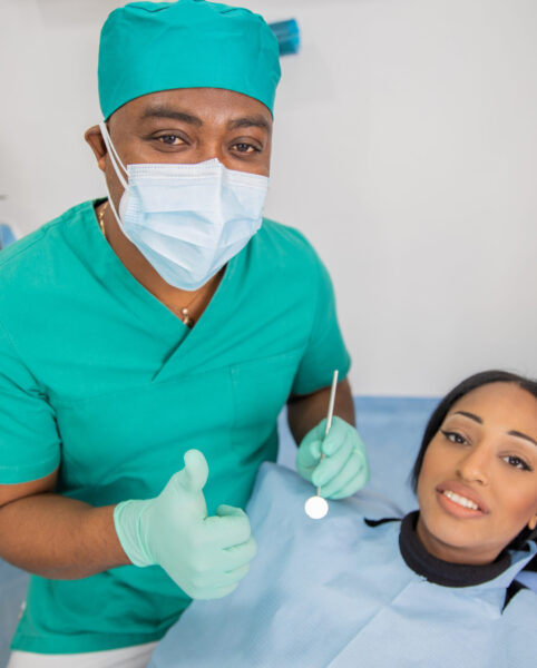 Happy dentist in his clinic during a visit with his patient does the thumbs up.